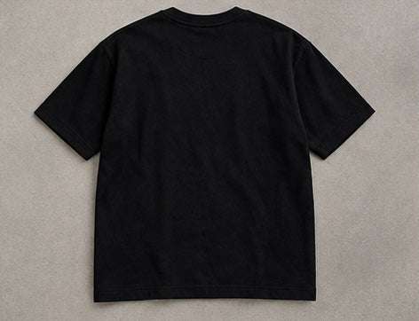 A plain black short-sleeve crewneck t-shirt shown from the back, laid flat on a textured gray background.