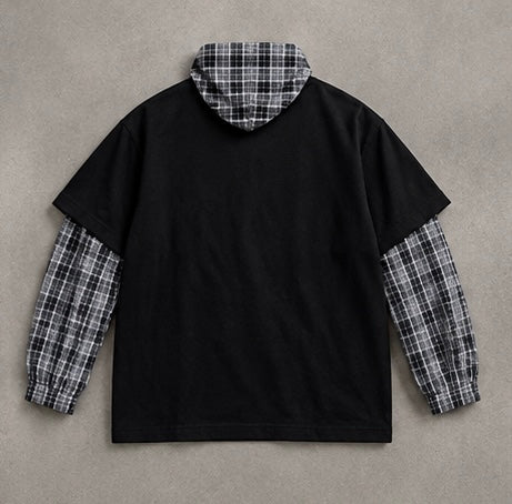 A black pullover hoodie with a black, white, and gray plaid hood lining and matching plaid sleeve cuffs, laid flat on a textured gray background.