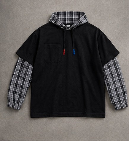 A black pullover hoodie with a plaid hood lining and matching plaid long sleeves, laid flat on a textured gray background.