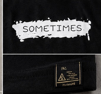 Close-up of a black garment featuring a white paint-splatter graphic with the word 'SOMETIMES' in black, plus a visible sewn-in brand label reading FA & Fuku.
