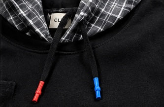 Close-up of a black hoodie with a black and white plaid hood lining and contrasting red and blue drawstring tips.