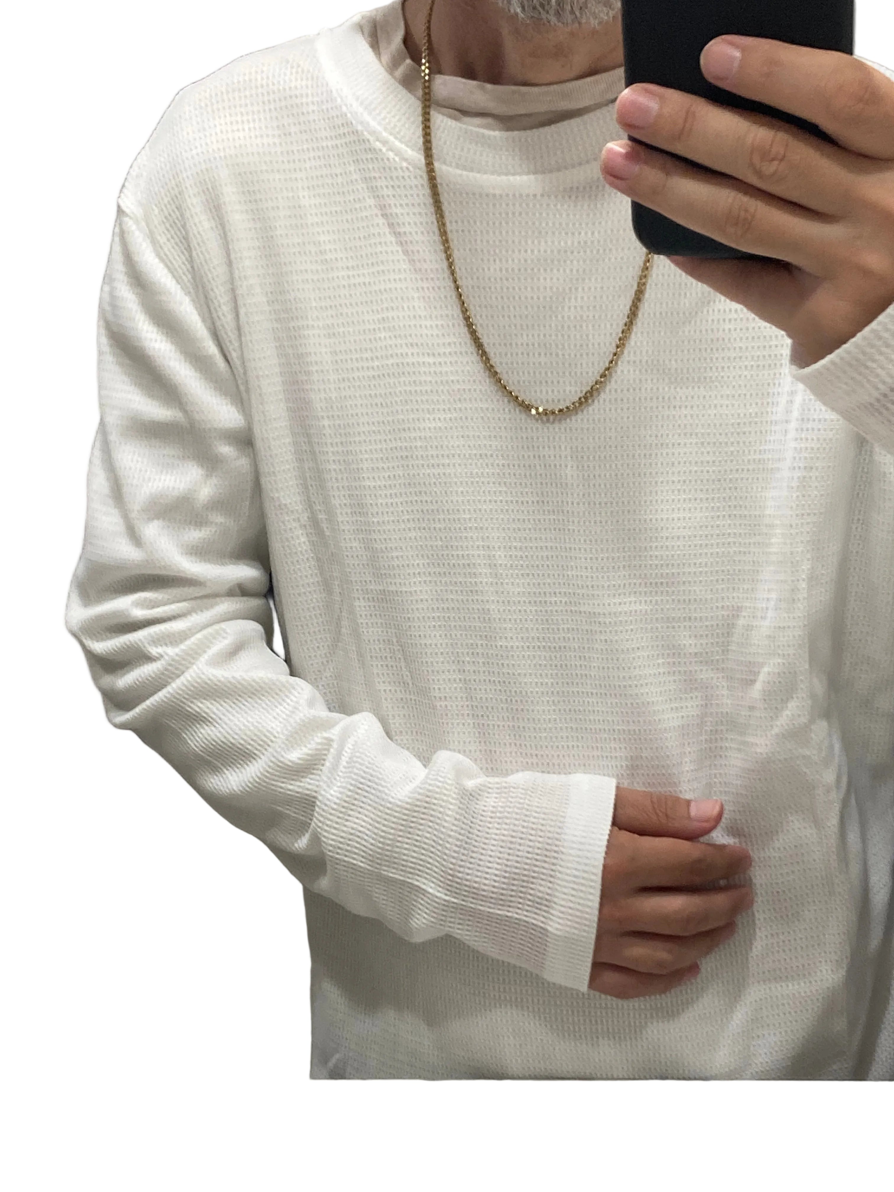 A person taking a mirror selfie wearing a white long-sleeve waffle-knit crewneck shirt, a gold chain necklace, and holding a black smartphone.