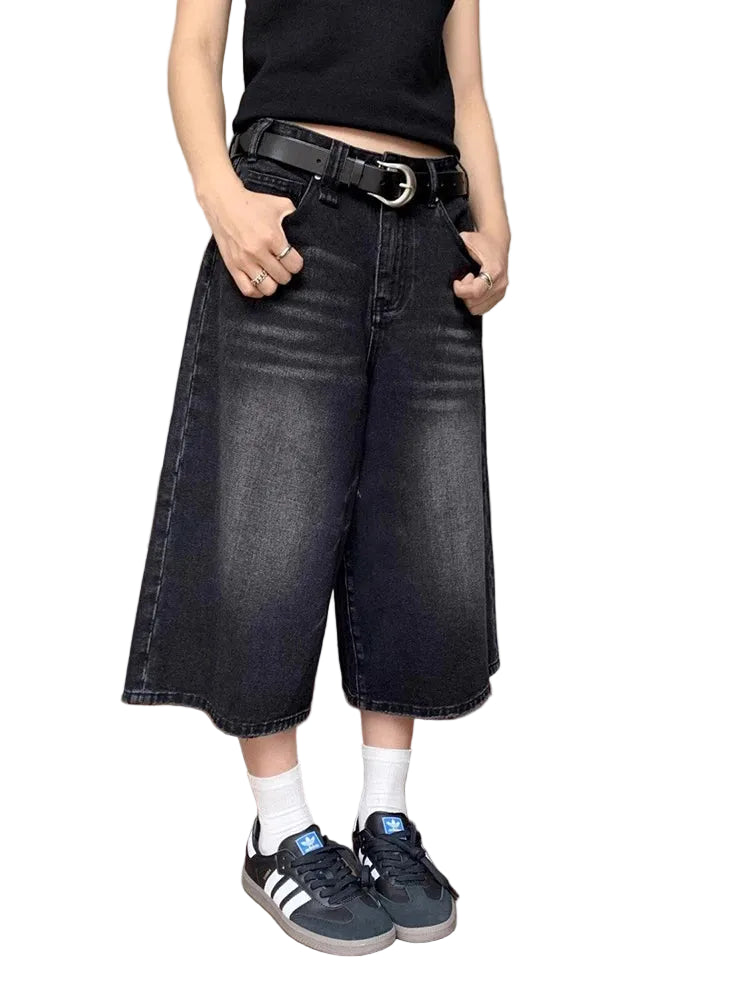 Person wearing black wide-leg jeans and Adidas sneakers in a bedroom setting.
