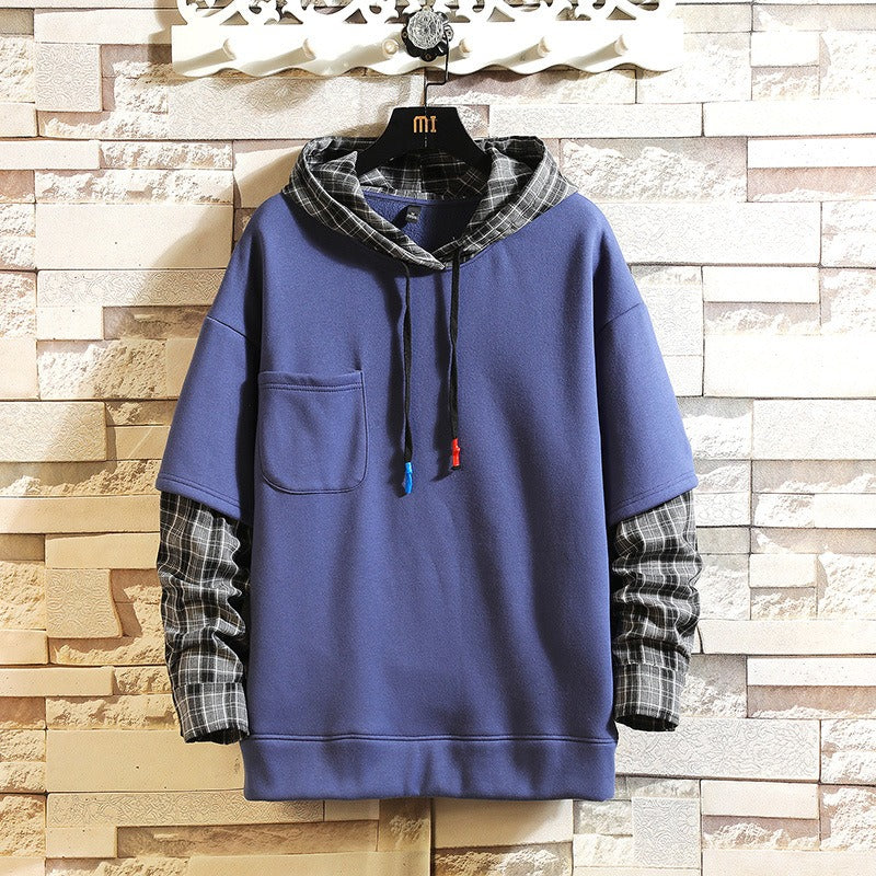 A blue pullover hoodie with a plaid hood lining and matching plaid rolled sleeves, hanging on a black hanger against a faux stone wall background.